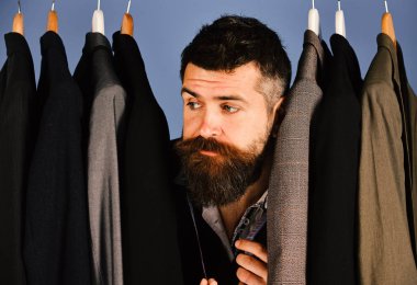 Tasarımcısı Giyim Askıları türler arasında gizler. Mavi arka plan üzerinde özel ceketler yakınındaki sıkılmış yüzle terzi,