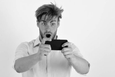 Adam şaşırmış yüzü ile cep telefonu tutar. Genç adam beyaz arka plan üzerinde izole cep telefonu ile fotoğraf çeker