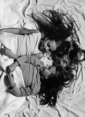 Beyaz ve pembe yatak çarşafları arka plan kızlar. Pembe pijamalı kız öğrenciler renkli yastıklar, üstten görünüm yaşamak. Çocukların neşeli yüzleri ve bağsız kıl ile yatakta yatmak. Pijama partisi ve çocukluk kavramı.