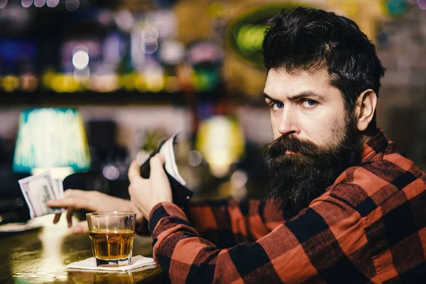 Man with strict face sit alone in bar or pub near bar counter. Rest and relax concept. Guy spend leisure in bar, defocused