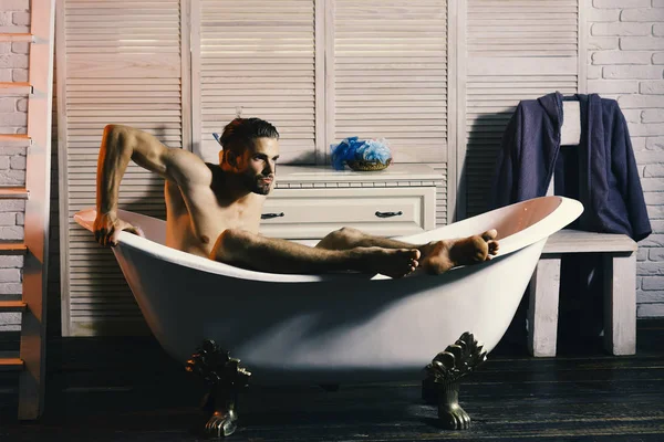 Guy in badkamer met toiletartikelen en trappen op de achtergrond. Seks en ontspanning concept: man met baard nemen bad — Stockfoto