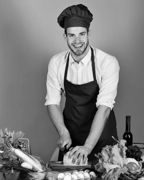 Mannen i kock hatt och förkläde nedskärningar kål. Cook fungerar i köket nära bord med grönsaker och verktyg. — Stockfoto