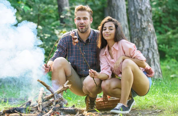 Couple roasting sausages on sticks nature background. Couple in love enjoy camping forest roasting sausage at bonfire. Camping and picnic. Traditional roasted food as attribute of picnic — Stock Photo, Image