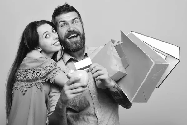 Man met baard houdt creditcard en piggy bank. Man met baard en dame met gelukkige gezichten boodschappen doen — Stockfoto