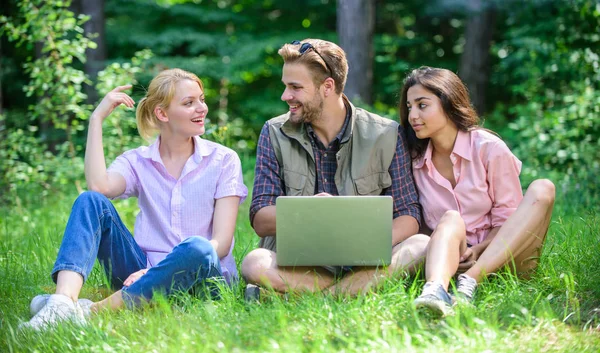 Les jeunes de l'entreprise passent leurs loisirs à l'extérieur avec un ordinateur portable. Amis travaillant avec un ordinateur portable à Green Meadow. Possibilité de freelance. Les technologies modernes offrent la possibilité de travailler dans toutes les conditions environnementales — Photo