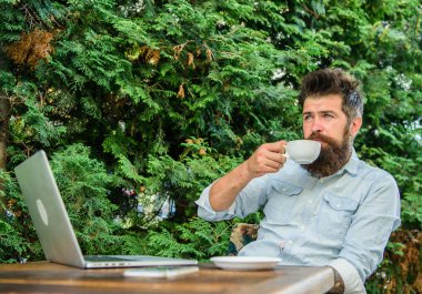 Hoş bir an. Hayattan zevk için zaman ayırın. Sakallı adam hipster yapmak kahve içmek için duraklatmak ve dizüstü bilgisayar ile oturup süre rahatla. Adam kahve rahatlatıcı Teras dalları arka plan içer. Aroma kapuçino