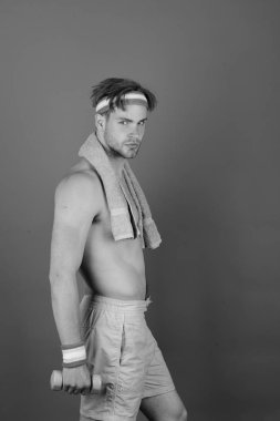 Çıplak gövdeli bir adam havluyu boynunda ve dambılında tutuyor.