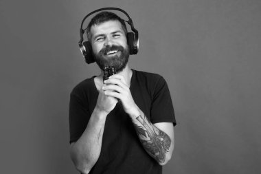 Sakallı DJ kulaklık takıyor, fotokopi çekiyor. Adam mikrofonu tutuyor.