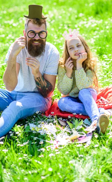 O pai e a filha sentam-se na relva no campo, fundo verde. Conceito Aristocrates. Criança e pai posando com óculos, coroa e chapéu superior atributos de cabine de fotos. Família passar o lazer ao ar livre — Fotografia de Stock