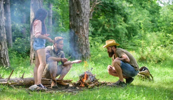 Add some wood to fire. Friends hang out near bonfire picnic. Company youth camping forest prepare bonfire for picnic. Company friends or family making bonfire in forest nature background