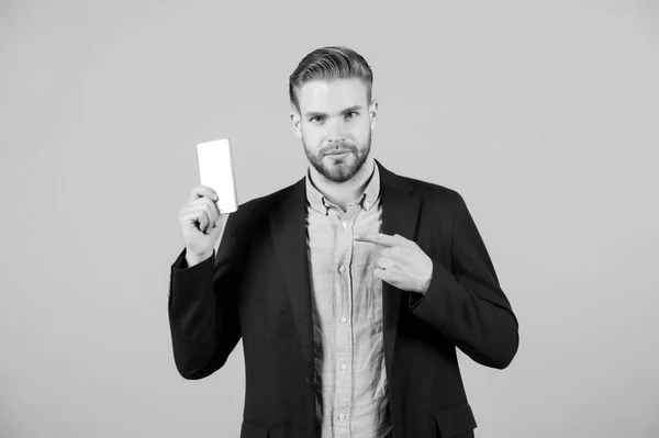 El hombre señala con el dedo el teléfono móvil. Empresario con barba en traje formal show smartphone. Presentación con anuncio o publicidad y promoción. Presentación del concepto de producto — Foto de Stock