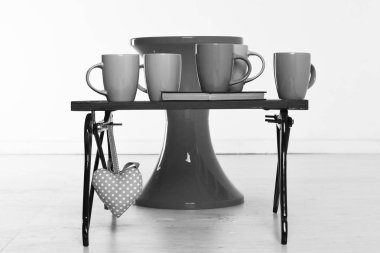 Pembe Kalp beyaz zemin üzerine kırmızı sandalye ve renkli bardak ve bir kitap ile siyah ahşap tepsi ter.