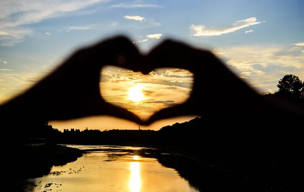 Romantic date ideas. Idea honeymoon travel. Vacation resort. Sunset sunlight romantic atmosphere. Hands in heart shape gesture symbol of love and romance. Heart gesture in front of sunset above river