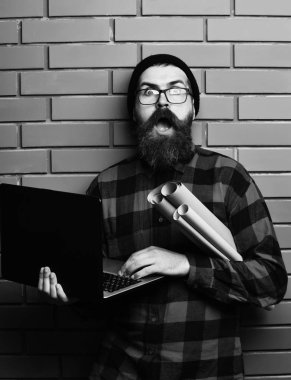 Kaba sakallı, beyaz tenli hippi elinde dizüstü bilgisayar ve el işi kâğıdı tutuyor.