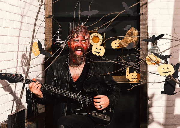 Man wearing scary makeup with Halloween pumpkins and bats decor