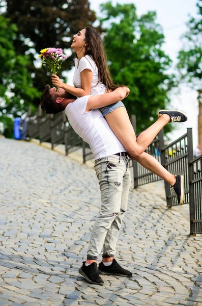 Verliebte Paare treffen sich zum Date im Park. Typ, der Freundin aufzieht. romantischer Date-Spaziergang. glücklich, sie zu sehen. Mann trägt Freundin in Händen, während sie Blumenstrauß auf l romantisches Date hält — Stockfoto