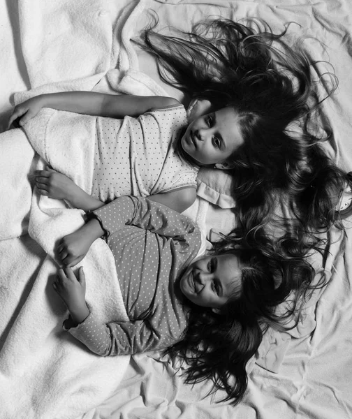 Schoolgirls in pink pajamas wallow on colorful pillows, top view