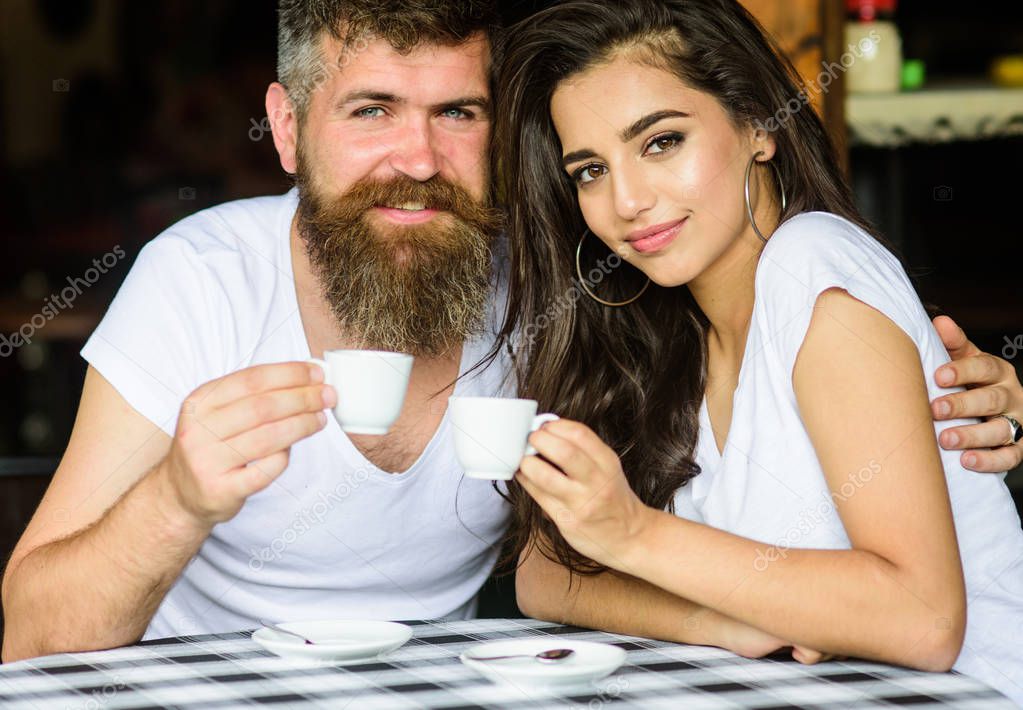 Couple in love drink black espresso coffee in cafe. Enjoy moment with cup of coffee drink. Man with beard and attractive happy smiling girl hugs and drinking coffee. Pleasant family moment
