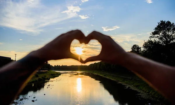 Conceito de memórias de verão. Os melhores lugares para encontros românticos. Sol luz do sol atmosfera romântica. Mãos masculinas em forma de coração gesto símbolo de amor e romance. gesto do coração em frente ao pôr do sol acima do rio — Fotografia de Stock