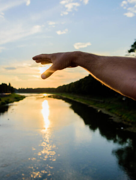 River sun reflection. Catch last sunbeam. Male hand pointing at sun in blue sky at evening time admire landscape. Capture moment to admire sunset nature beauty. Enjoy sunset above river surface
