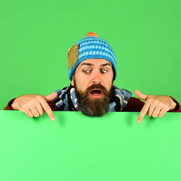 Man in warm hat points down on green background