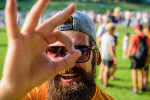 Будьте уверены на летних каникулах. Мужчина бородатый на фоне толпы на берегу реки. Забронируйте билеты на летний фестиваль заранее. Фестиваль посещений хипстеров. Мужчина веселое лицо смотрит сквозь хорошо жест

