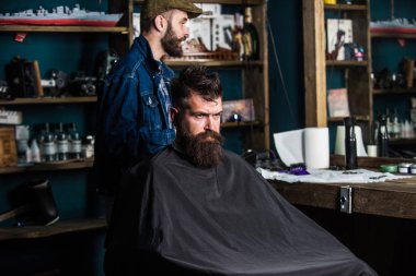 Hipster istemci Başlarken saç kesimi. İstemci ile sakal düzeltme veya bakım için hazır. Sakallı adam kesme makinesi sınıf değiştirme Kuaför bekleyen siyah pelerin ile kaplı. Saç kesimi işlem kavramı
