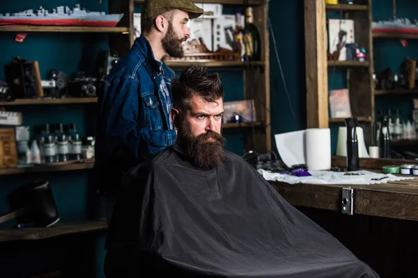 Um cliente Hipster a cortar o cabelo. Cliente com barba pronta para aparar ou arrumar. Homem com barba coberta com capa preta esperando enquanto o barbeiro muda de categoria clipper. Processo de corte de cabelo conceito — Fotografia de Stock