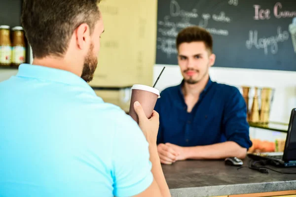 男は、バック グラウンドでコーヒー バリスタ男スタンド付き紙コップを保持しています。クライアントは、彼の飲み物を得た。エネルギーの sip があります。髭男のクライアントでは、紙コップのコーヒーをお楽しみください。モダンなカフェで便利なオプションを行く飲み物 — ストック写真