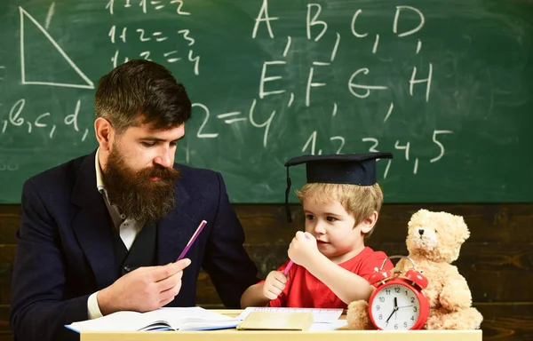 Hometask のコンセプトです。正式な摩耗と鏝板の教室で、背景に黒板に生徒の教師。Hometask、男の子に助けをチェックの父の息子。先生と勉強熱心な子供 — ストック写真