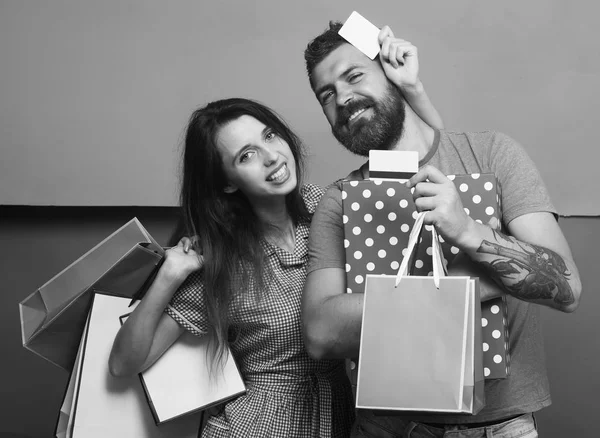 El tipo con barba y la señora con caras felices hacen compras. Pareja en el amor abrazos y sostiene caja y bolsas de compras — Foto de Stock