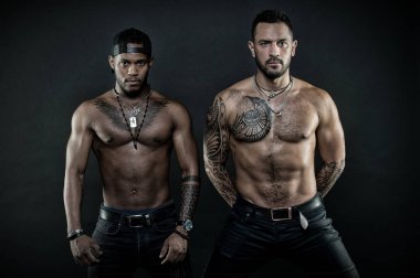 Sporcular fit ile karanlık kot giyen organları, sağlık ve vücut bakım kavramı. Dövmeli sandıkları ve kolları ile Afrika ve beyaz erkekler. Ciddi yüzü siyah arka plan üzerine izole olan erkekler