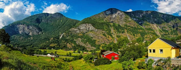 Pintoresco pueblo con pequeñas casas, cabañas, en las montañas rocosas montañosas cubiertas de árboles verdes y hierba en el día de verano soleado sobre el fondo cielo azul nublado. Norway. vagabundeo . —  Fotos de Stock