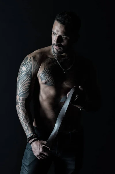 Modelo de moda con cinturón de cuero en jeans. Hombre con diseño de tatuaje en la piel. Hombre barbudo con torso muscular. Deportista con brazo y pecho tatuados. Cuidado del cuerpo con fitness y deporte en filtro vintage — Foto de Stock