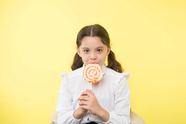 Yetersiz beslenme yaygın bir sorundur. Kız öğrenci üniforması lolipop şeker sarısı arka plandan hoşlanıyor. Şirin kız at kuyruklu, saç stili tatlı lolipop yiyor. Uygun oranlarda şekerleme. Tamam.