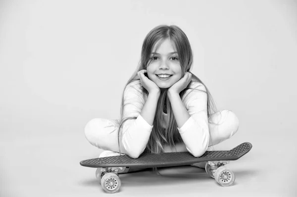 Дитина на скейтборді лежить на рожевому тлі. Дитячий ковзаняр посміхається з дошкою. Маленька дівчинка посміхається з дошкою для катання. Дитячий спосіб життя та активні ігри. Спортивна активність та енергія, пунш пастель — стокове фото