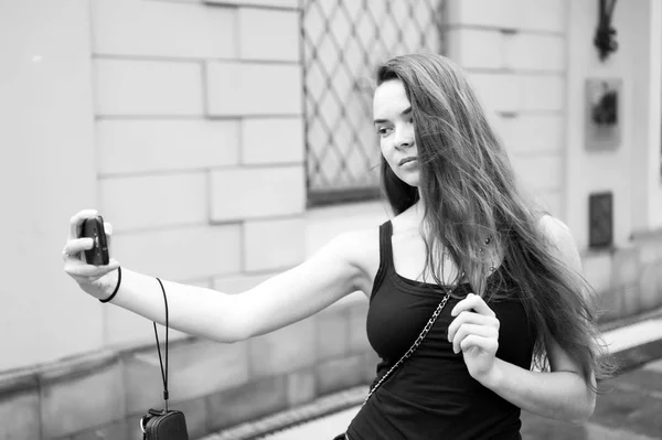 Kobieta zrobić selfie z telefonu komórkowego na ulicy. Kobieta z długimi włosami używać smartfona na świeżym powietrzu. Dziewczyna z wyglądem mody i zmysłowe piękno. Koncepcja wakacji letnich i podróży — Zdjęcie stockowe