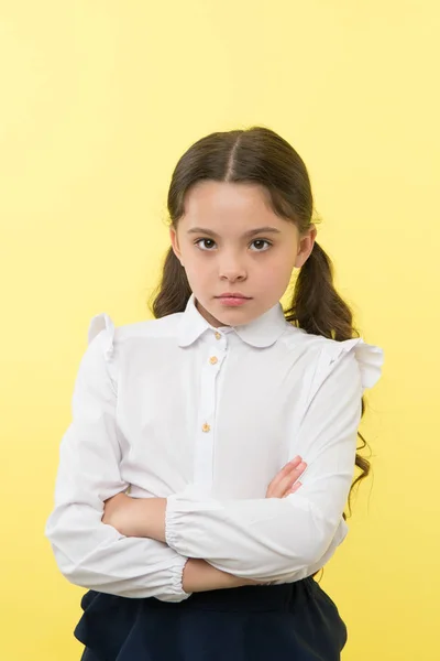 She does not agree with you. Girl serious face offended yellow background. Kid unhappy looks strictly. Girl school uniform folded arms on chest looks serious. Sensitive girl not want to talk — Stock Photo, Image