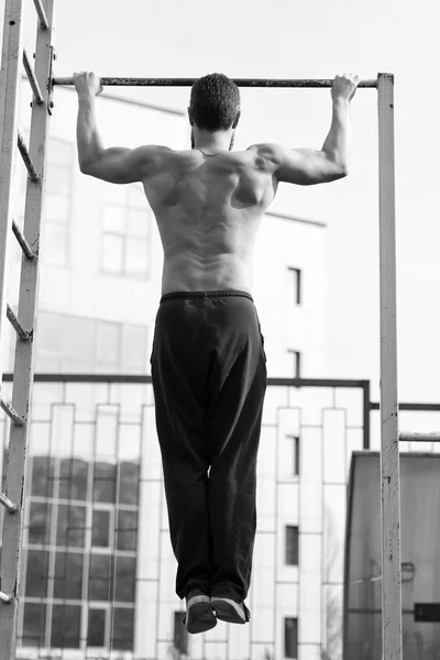 Hombre hacer barbilla ups al aire libre. El deportista se detiene en el estadio. Atleta con el torso en forma y manos fuertes en la barra. Ejercicios de bar con mentón. Actividad de entrenamiento y entrenamiento. Fuerza o potencia y deporte, vista trasera —  Fotos de Stock