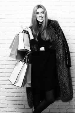 Birçok renkli paket beyaz tuğla duvar studio arka plan üzerinde tutarak. kürk moda seksi kadın