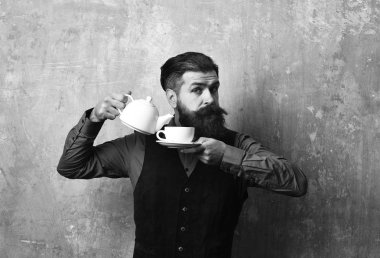 Sakal ve bıyık tutan çay bej duvar arka plan üzerinde olan adam. Garson pot beyaz çay fincan içine çay dökülen