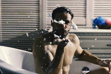 Adam banyoda tuvalet malzemeleri ve arka plan merdivenlerde köpükle kaplı. Erotik kavram olarak banyo küvetinde çıplak olarak oturan maço