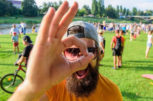 Мужчина веселое лицо смотрит через хорошо жест. Мужчина бородатый на фоне толпы на берегу реки. Забронируйте билеты на летний фестиваль заранее. Будьте уверены на летних каникулах. Фестиваль посещений хипстеров
