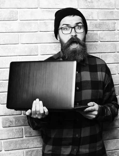 Óculos no fundo do estúdio parede de tijolo bege. Barbudo brutal caucasiano hipster segurando laptop — Fotografia de Stock