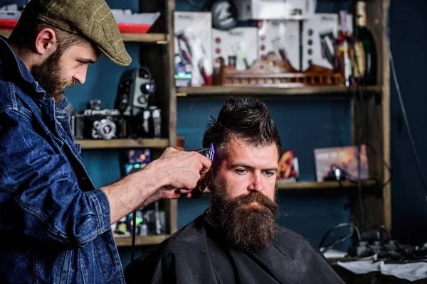 Barbiere con taglierina che taglia capelli su tempio di cliente. Concetto di stile di vita hipster. Un cliente hipster che si taglia i capelli. Barbiere con tagliacapelli lavora su acconciatura per barbuto uomo barbiere sfondo — Foto Stock