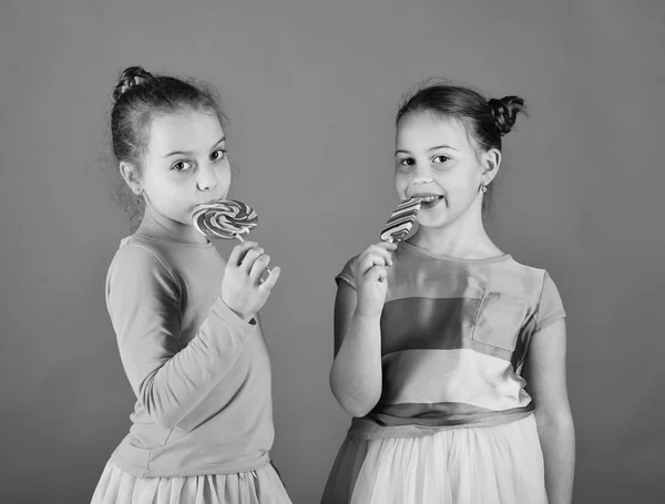 Kinder essen große bunte süße Karamellen. Schwestern mit runden, lang geformten Lutschern. Mädchen mit glücklichen Gesichtern — Stockfoto