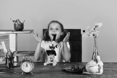 Pembe bir arka plan üzerinde çocuk ve okul malzemeleri. Sarı çiçekler, kırmızı saat, meyve ve renkli ileti örneği ile masada kız öğrenci. Kız sürpriz yüz ile mikroskop kullanır. Çalışma odası ve güzellik kavramı