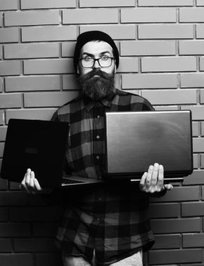 Sakallı adam, uzun sakallı. Kahverengi tuğla duvarlı stüdyo arka planında şapka ve gözlüklü kırmızı siyah kareli tişörtlü, traşsız hippi..