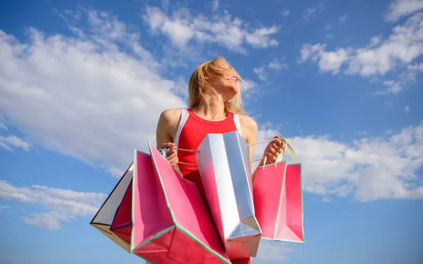 Flicka nöjd med köp. Kvinna röd klänning bär gäng påsar blå himmel bakgrund. Känn dig fri köpa allt du vill ha. Shopping bästa sättet att öka humör. Slutligen köpte favoritmärken — Stockfoto