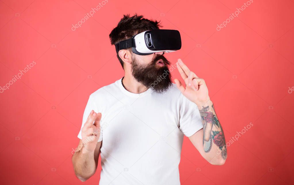 Man bearded hipster with virtual reality headset on red background. Shooting VR game. Man hand gesture as gun play shooter game in VR glasses. First person shooter shows how addictive VR could be